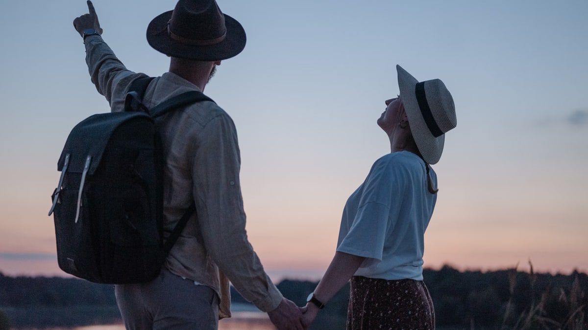 Romantic couple holding hands while watching a sunset at a serene lakeside location, embracing nature.