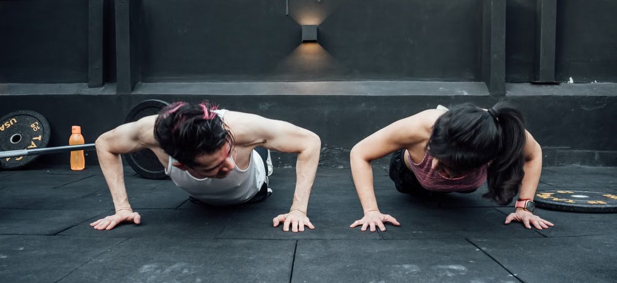 Two adults doing push-ups in an indoor gym setting in Mexico City, promoting a fit and healthy lifestyle.